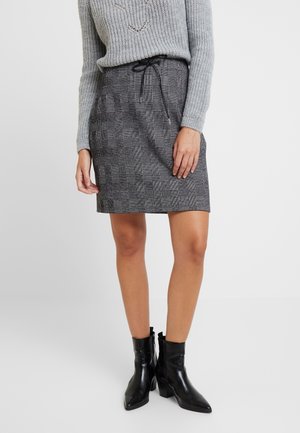 Jupe à carreaux gris avec ceinture à cordon, design longueur genou et tissu texturé, associée à des bottines noires à la cheville.