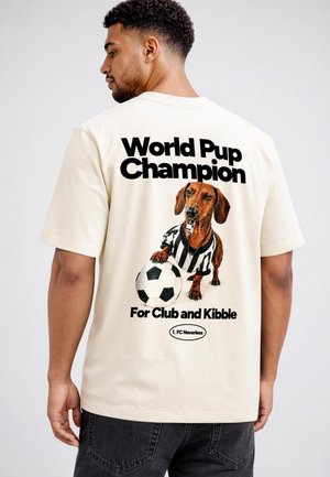 Man wearing a white t-shirt with a graphic of a dog in a referee shirt holding a soccer ball and text reading "World Pup Champion" on the back.