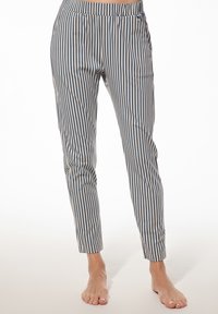 Blotevoeten persoon in blauwe en witte verticaal gestreepte slim-fit broek staand op een lichte ondergrond.