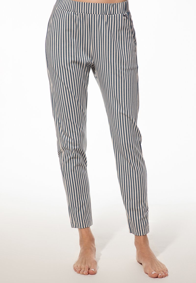 Blotevoeten persoon in blauwe en witte verticaal gestreepte slim-fit broek staand op een lichte ondergrond.