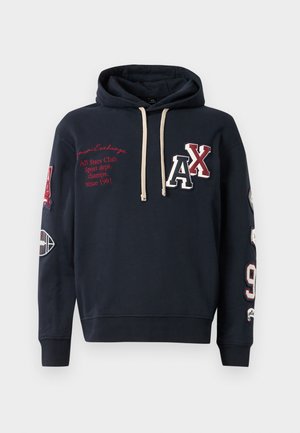 Sweatshirt à capuche bleu marine avec logo et texte sur le devant, présentant des cordons beige, des détails brodés et des accents à motifs sur les manches.