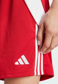 Rote Trainingsshorts mit drei weißen Streifen an der Seite. Das Material wirkt glatt; ein weißes Adidas-Logo befindet sich in der Nähe des Saums.