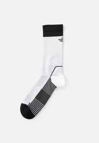 Calcetín deportivo blanco con puño y punta negros. Presenta texturas variadas, incluyendo rayas y un patrón hexagonal en el pie.