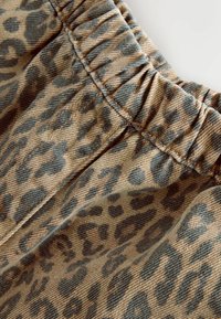 Látka s leopardím potiskem mísí odstíny béžové a hnědé s nařaseným pasem. Textura je měkká s denimovým vzhledem.
