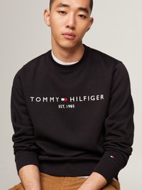 Schwarzer Baumwollpullover mit "TOMMY HILFIGER"-Logo in Weiß und roten sowie blauen Akzenten, gerippten Bündchen und rundem hals.