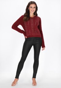 Bordowy sweter w splot kabelkowy z akcentami z kryształków, zestawiony z czarnymi dopasowanymi legginsami i przezroczystymi sandałami na obcasie na białym tle.