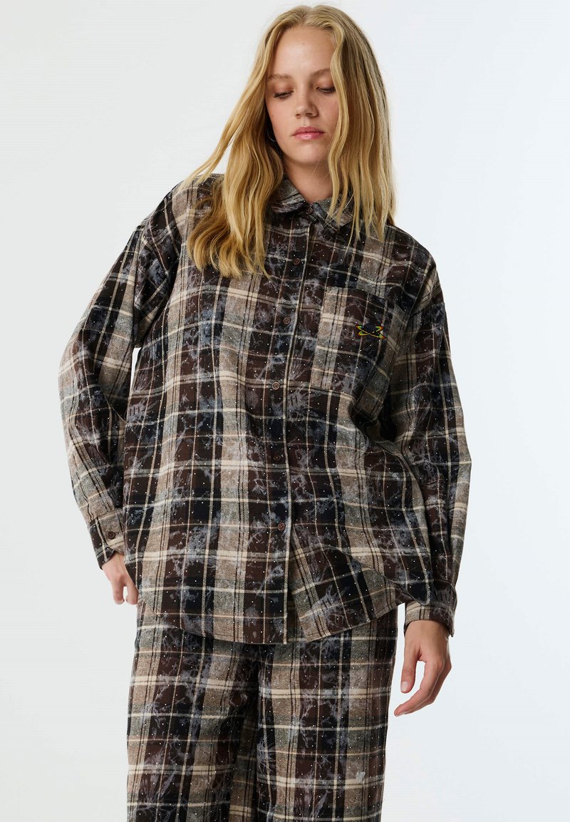 Camicia a quadri con bottoni in marrone e crema, dal taglio rilassato. Presenta maniche lunghe, colletto e un piccolo logo sul petto.