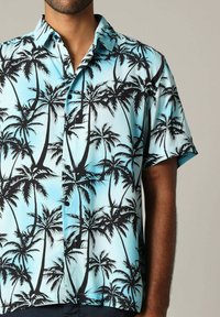 Korte mouwen button-up shirt met een lichtblauwe achtergrond en zwarte palmbomenpatronen in een relaxte pasvorm. Gemaakt van een lichte stof.
