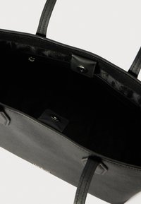 Sac fourre-tout noir avec deux poignées texturées, fermeture à pression et intérieur doublé. Présente un extérieur lisse et un design épuré.