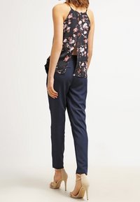 Blusa sin mangas negra con estampado floral y espalda abierta, combinada con pantalones tapered azul marino y zapatos de tacón nude.