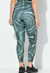 Leggings de talle alto en verde oscuro con un patrón espiral en azul claro. Fabricados con un material elástico y suave, con un diseño ajustado.