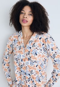 Langärmliges Hemd mit floralem Muster in den Farben Pfirsich, Blau und Marineblau. Verfügt über eine Tasche, einen Kragen und eine lässige Passform aus leichtem Stoff.