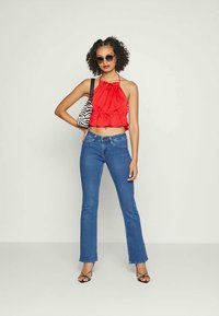 Top halter vermelho com design franzido, calças azuis de boca de sino e sapatos de salto pretos com tiras. Bolsa de zebra e óculos de sol redondos completam o visual.