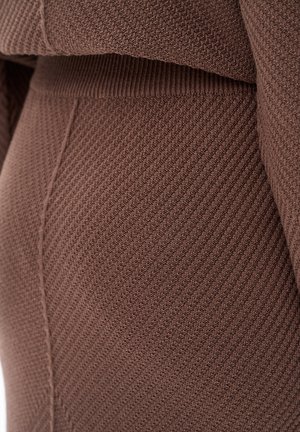 Brązowa dzianina o prążkowanej fakturze z pionowymi liniami. Ubranie ma gładki pas i obcisły krój.