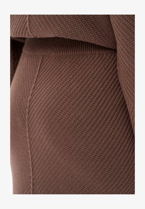 Brązowa dzianina o prążkowanej fakturze z pionowymi liniami. Ubranie ma gładki pas i obcisły krój.