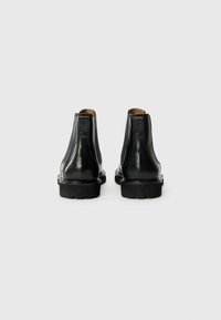 Black leather Chelsea boots with a smooth finish, elastic side panels, and a chunky rubber sole; back view shows stitching detail.