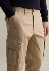 Beige Cargo-Hosen aus Baumwolle mit entspannter Passform. Verfügt über Seitentaschen und eine glatte Textur. Bund mit Knopfverschluss.