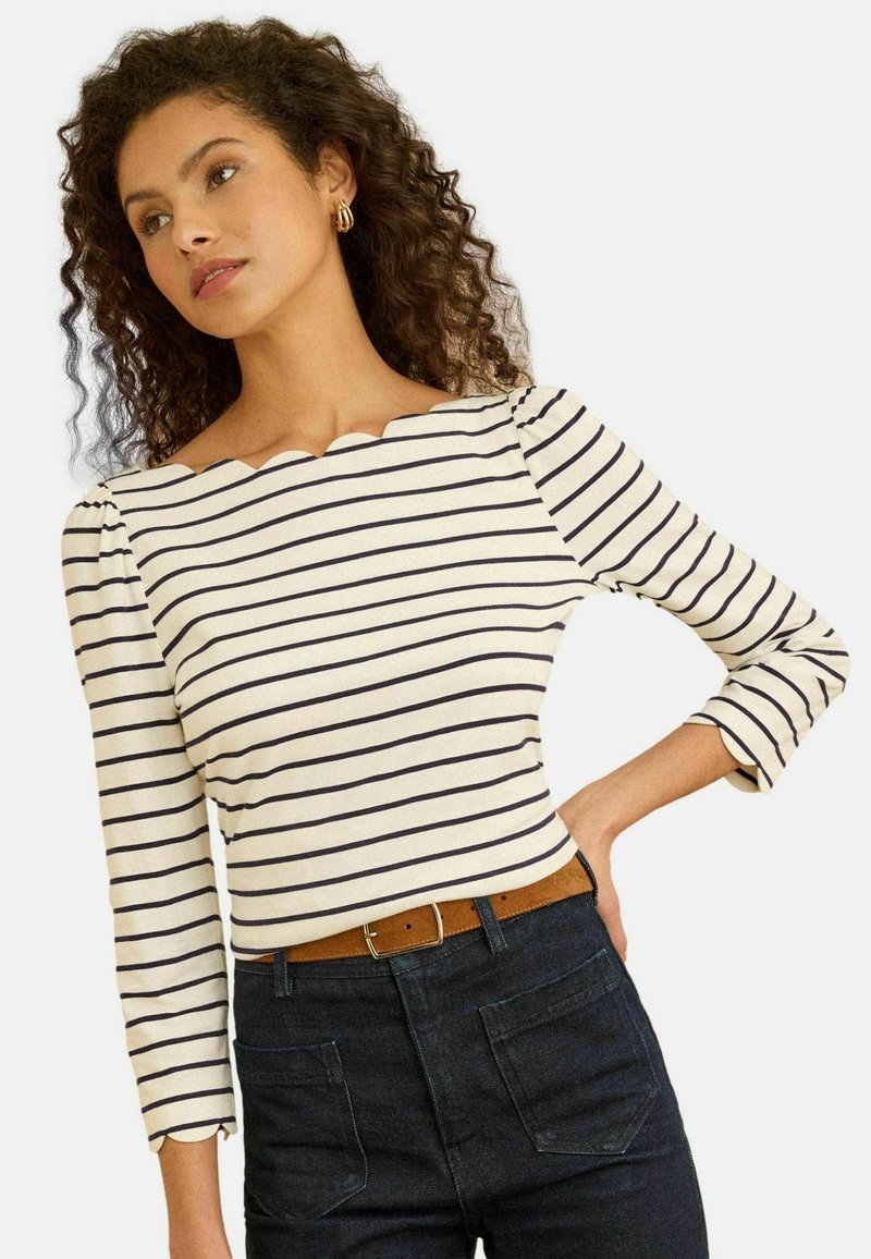 Pruhovaný top s dlhým rukávom a vrúbkovaným výstrihom, vyrobený z ľahkého materiálu. Má biely základ s námorníckymi pruhmi a priliehavý strih.