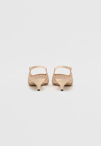 Paire d'escarpins beige à bride arrière et petit talon avec motif texturé sur les côtés, vus de dos sur un fond clair uni.