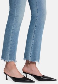 Schwarze Leder-Mules mit spitzer Zehenpartie und Stiletto-Absatz. Getragen mit hellblauer, ausgewaschener Denim, die ausgefranste Säume hat.