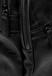 Mochila de cuero negro con una superficie texturizada, que cuenta con un cierre central con cremallera y un bolsillo frontal adicional con cremallera lisa.