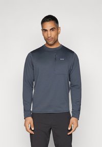 Long-sleeve, navy blue shirt in a smooth synthetic fabric, featuring a small zip pocket on the chest and a ribbed collar.