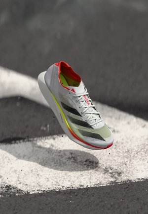 Running shoe with a white and grey mesh upper, red accents, elongated shape, lightweight design, and a brightly colored cushioned sole.