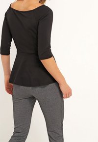 Černý peplum top s širokým lodním výstřihem a tříčtvrtečními rukávy, doplněný o přiléhavé šedé kalhoty. Hladká látka s mírným leskem.