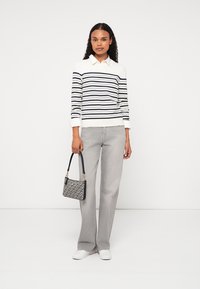 Stripet langermet topp med hvite og marineblå striper, kombinert med grå utslåtte jeans og hvite sneakers, holder en mønstrete håndveske.