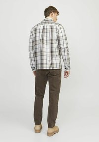 Geruite shirt in wit, bruin en marineblauw, met lange mouwen en knoopmanchetten, met recht gesneden bruine broek en beige schoenen.