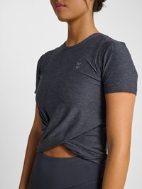 Kobieta ubrana w ciemnoszary, krótki rękaw, sportowy top z wiązaniem z przodu i dopasowane legginsy z wysokim stanem, pokazana od szyi do bioder.