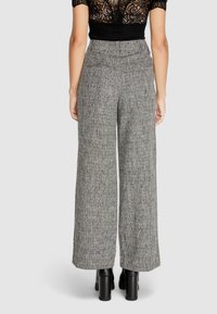 Pantaloni a gamba larga grigi di tessuto texturizzato con vita alta. Il tessuto presenta un motivo sottile e sono abbinati a stivali neri con tacco a blocco.