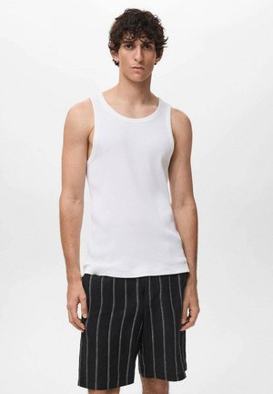 Débardeur blanc à côtes avec un col rond associé à un short rayé noir et blanc. Le modèle se tient devant un fond blanc uni.