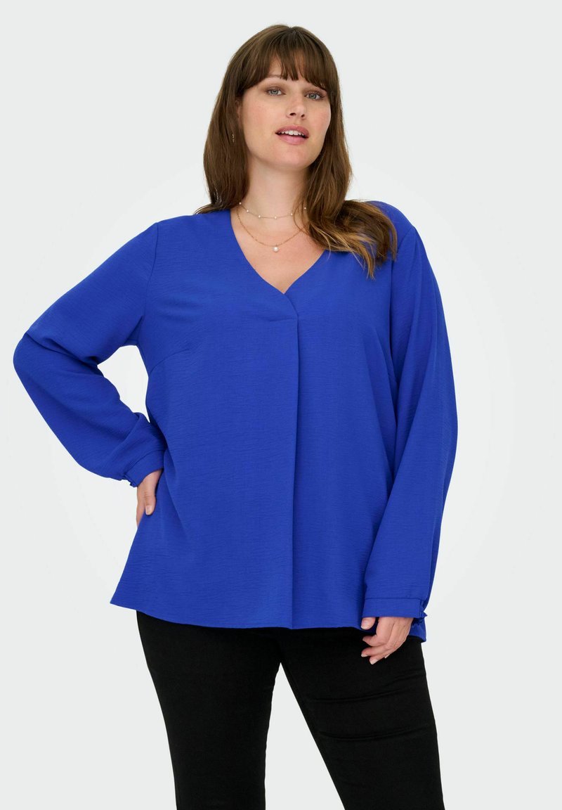 Langärmlige, tiefblaue Bluse mit V-Ausschnitt und strukturiertem Stoff, die eine lockere Passform und seitliche Schlitze am Saum hat.