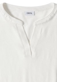 Chemise en coton blanc avec un décolleté en V et un petit col montant, comportant une étiquette de marque "CECIL" à l'intérieur du col.