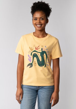 T-shirt en coton jaune avec un graphic de sirène verte entourée de motifs floraux abstraits en rose, violet et bleu. Manches courtes, col rond.