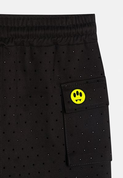 Black fabric with small evenly spaced holes, featuring a pocket with a yellow patch showing a three-eyed monster face with fangs.