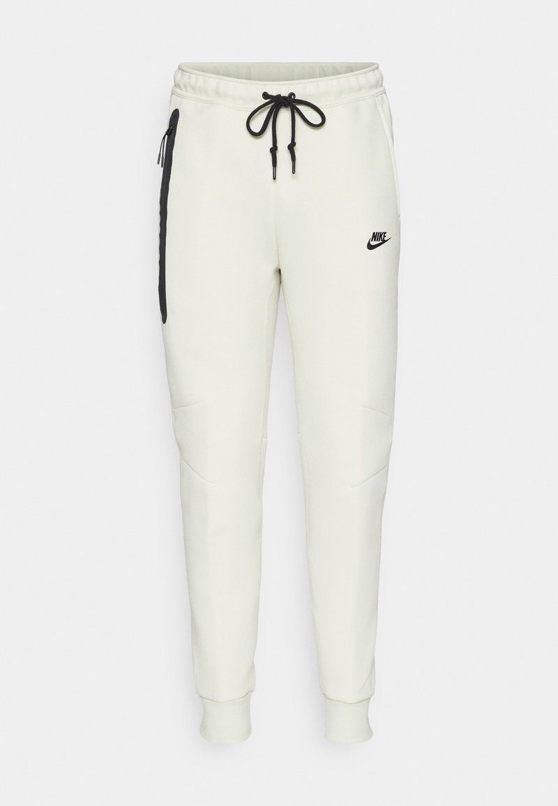Nike Jogginghosen in hellem Creme, mit einem schwarzen Logo, verstellbarem Kordelzug, seitlichen Reißverschlusstaschen und schmalem Bein-Design.