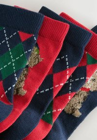 Värvilised mustrikandjal sokid, millel on segu tumseebrist, punast ja roheline ning argyle-muster koos tekstuuriga pruuni karu detailiga.