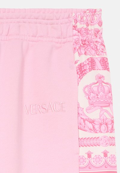 Pantalones de chándal rosas con cintura elástica, tejido texturizado y un patrón floral decorativo en un lado. "VERSACE" está bordado en la parte frontal.