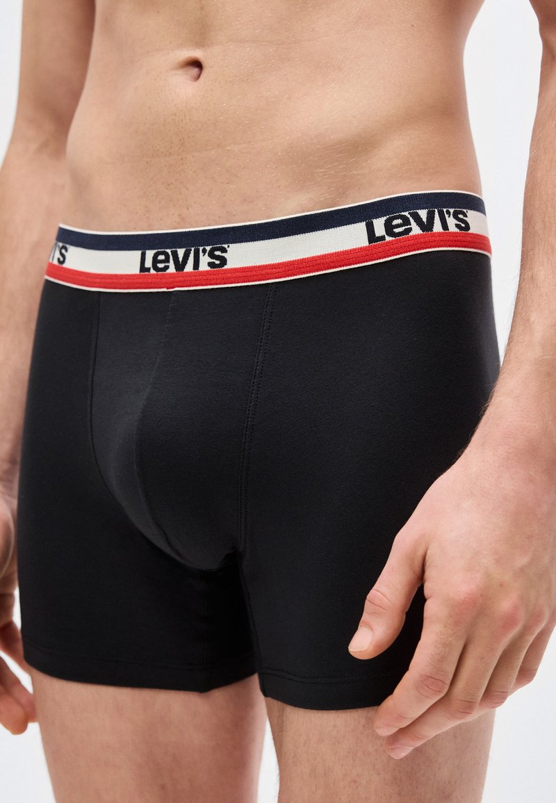 Close-up of a male torso wearing black Levi's boxer briefs with a navy, white, and red waistband featuring the Levi's logo.