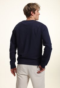 Sudadera azul marino con cuello redondo y mangas largas, hecha de un material suave. Presenta puños y cintura acanalados.