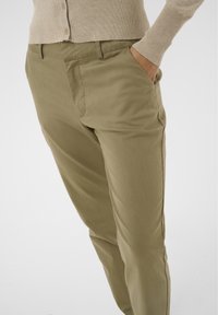 Pantalon kaki en tissu doux et texturé ; il présente une coupe ajustée, des poches latérales et une taille lisse pour le confort.