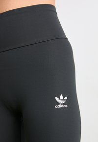 Crne aktivne tajice od glatkog, rastezljivog materijala. Imaju visoki pojas i bijeli Adidas trefoil logo na butini.