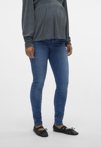 Blå skinny jeans i denim med midjehöjd och subtila blekningar, kombinerat med svarta ballerina-skor med en samlad design.