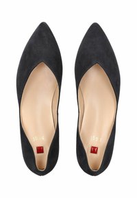 Černé semišové baleríny s špičatou špicí, s výřezovým designem a béžovou stélkou. Mají malé červené akcenty na podrážce a decentní zlaté logo.