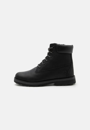 Stivaletto alla caviglia in pelle nera con colletto imbottito, chiusura con lacci frontale e suola robusta, mostrato dal lato esterno su sfondo uniforme.