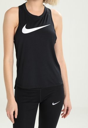 Kvinna i svart ärmlös Nike-top och svarta leggings, båda med vita Nike-swoosh-logotyper.