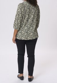 Bluzka w kwiaty w kolorze czarnym i kremowym z rękawami 3/4, zestawiona z dopasowanymi czarnymi spodniami i czarnymi płaskimi butami. Teksturowana tkanina.