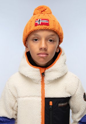Beanie arancione lavorato a maglia con pompon e una patch rossa e bianca. Giacca in pile bianca con zip arancione, maniche blu e dettaglio della tasca nera.